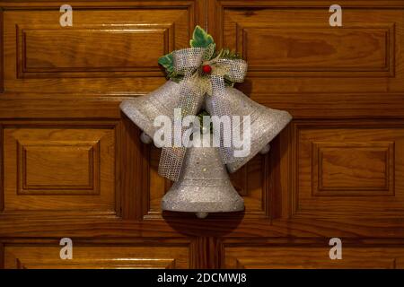 Campane d'argento appese all'ingresso della porta di legno. Ornamenti di Natale a casa. Decorazioni in stile ghirlande tradizionale Foto Stock