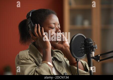 Ritratto di talentuosa donna afroamericana che canta al microfono e indossa le cuffie mentre si registra musica in studio, copia spazio Foto Stock