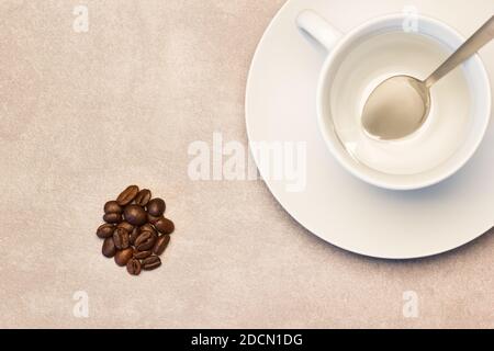 Un mazzo di chicchi di caffè tostati che si stendano accanto a un caffè tazza con cucchiaio Foto Stock