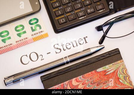 CO2-Steuer auf Papier zwischen Kugelschreiber, Euro Bankoden, Taschenrechner, Notizbuch und smartphone Foto Stock
