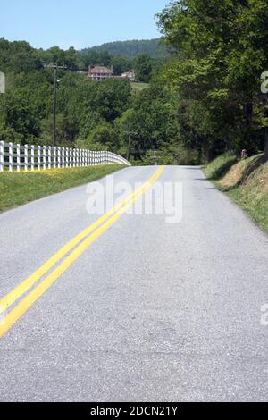 Strada di campagna a due corsie in Virginia, Stati Uniti. Proprietà rurale delimitata da lunga recinzione in vinile, con vista sulle montagne. Foto Stock