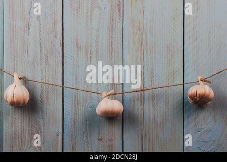 Tre teste intere di aglio appese sullo spago uno sfondo di legno rustico blu Foto Stock