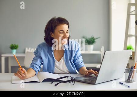 Un'insegnante sorridente conduce una lezione online tramite chat video sul computer portatile mentre si è a casa. Foto Stock