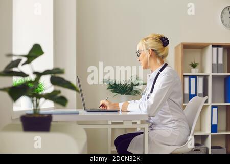 Dottoressa seduto sul posto di lavoro di fronte a un computer portatile in un ufficio ospedaliero e di scrittura. Foto Stock