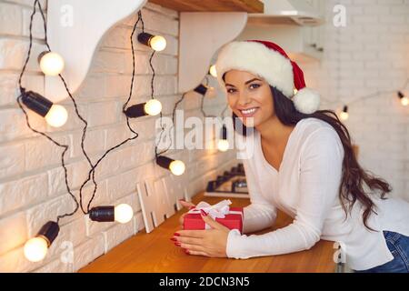 Sorridente bella giovane donna nel cappello di vacanza di Santa seduta con Regalo di Natale Foto Stock