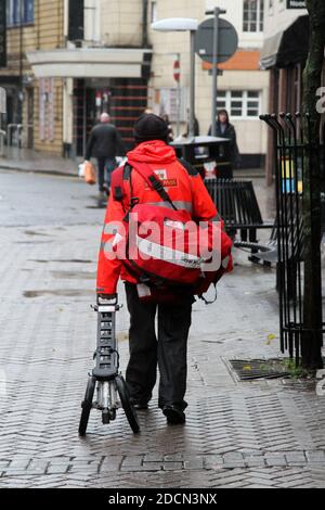 Ayr, Ayrshire, Scozia, Regno Unito. Scene di strada osservazioni candide. Postino con carrello a piedi lontano dalla macchina fotografica Foto Stock