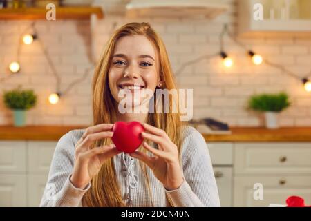 Felice giovane donna che tiene il cuore rosso, guardando la macchina fotografica e dicendo grazie per il presente Foto Stock