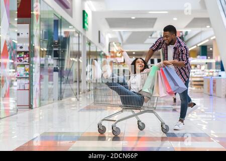 Allegro uomo nero tirando carrello con la sua ragazza dentro, divertendosi Foto Stock