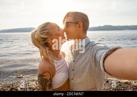 Felice giovane coppia Kissing e prendendo Selfie a Beach Foto Stock