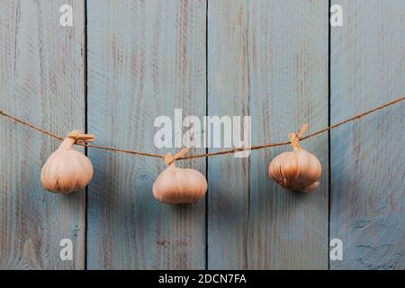 Tre teste intere di aglio appese sullo spago uno sfondo di legno rustico blu Foto Stock