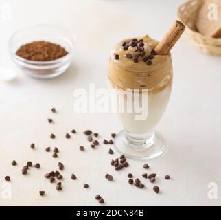 Un primo piano di un bicchiere di caffè Dalgona sul tavolo con gocce di cioccolato su di esso Foto Stock