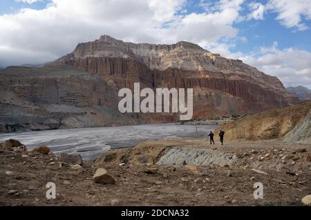 Tour turistico e facchino che cammina lungo le rive del fiume Kali Gandaki, sullo sfondo delle montagne dell'Himalaya. Trekking alla zon chiusa Foto Stock