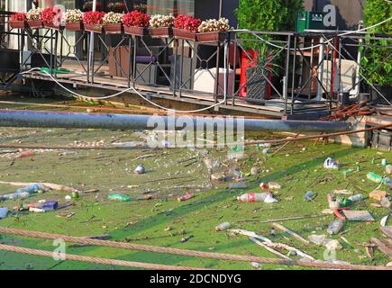 Problemi ambientali. Bottiglie di plastica e rifiuti galleggianti sull'acqua del fiume di fronte alla zattera della città. Problema irresponsabile; Foto Stock