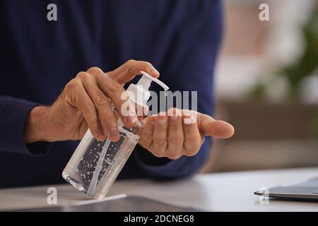 Primo piano di un uomo maturo irriconoscibile che utilizza l'igienizzatore per le mani mentre lavi le mani sul posto di lavoro, spazio per la copia Foto Stock