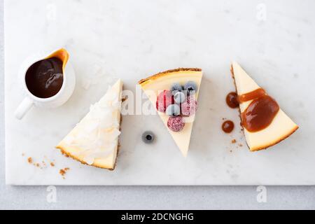 Assortimento di cheesecake con guarnizioni diverse. Cheesecake al cocco, cheesecake al caramello e fetta di cheesecake newyorkese con frutti di bosco surgelati. Foto Stock