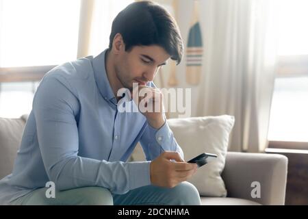 Uomo d'affari pensivo che tiene il cellulare pensando all'offerta ricevuta via e-mail Foto Stock