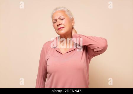 Donna ispanica anziana che tiene il collo nel dolore e nel disagio. Scatto in studio Foto Stock