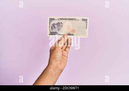 Mano ispanica con una banconota da 5000 yen giapponese su sfondo rosa isolato. Foto Stock