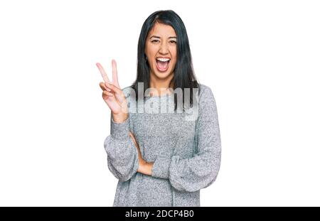 Bella giovane donna asiatica che indossa abiti casual sorridendo con felice faccia che si inarricava alla macchina fotografica facendo segno di vittoria. Numero due. Foto Stock