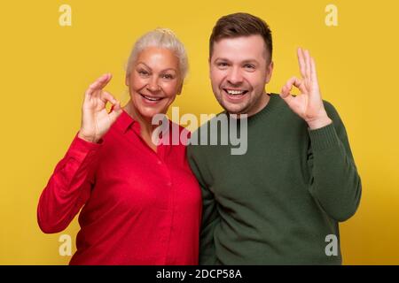 Uomo e donna mature sorridenti, madre e figlio che mostrano il segno OK con due mani. Foto Stock
