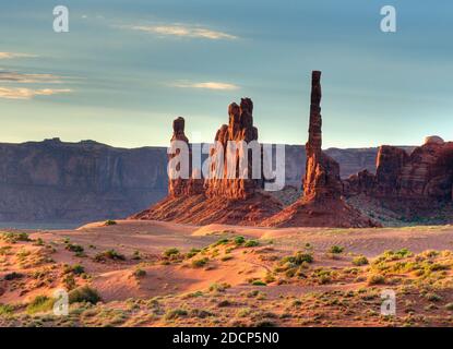 Vista sul Totem Pole nelle dune di sabbia di La Monument Valley Arizona al mattino su un sole Giorno d'estate con un cielo blu chiaro e alcuni Nuvole Foto Stock