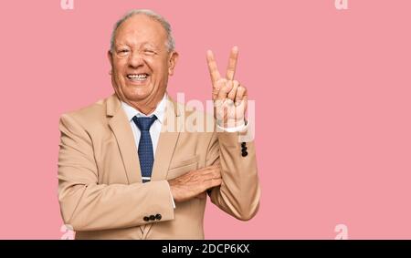 Uomo caucasico senior che indossa il costume da lavoro e legare sorridendo con felice faccia che si inarricia alla macchina fotografica facendo segno di vittoria. Numero due. Foto Stock