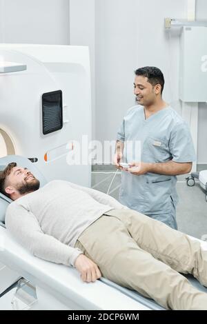 Felice medico maschile misto-razza in uniforme medica e sorridente sopportato paziente Foto Stock