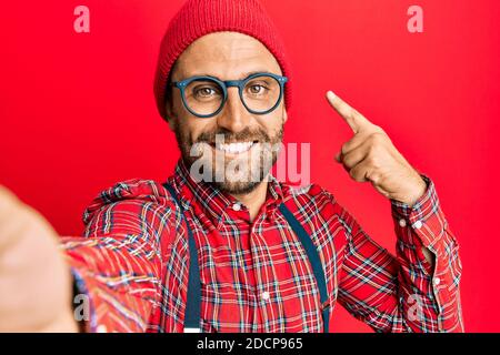 Bell'uomo hipster con barba scattando una foto selfie con smartphone sorridente che punta con mano e dito Foto Stock