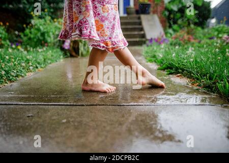 primo piano di un piccolo bambino a piedi nudi che danzava sul piano anteriore sotto la pioggia Foto Stock