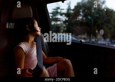 Una bella bambina che indossa la cintura di sicurezza dorme in un auto al crepuscolo Foto Stock