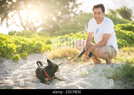 Giovane squadra maschile in forma sulla spiaggia con il suo piccolo Cane nero alle Hawaii Foto Stock