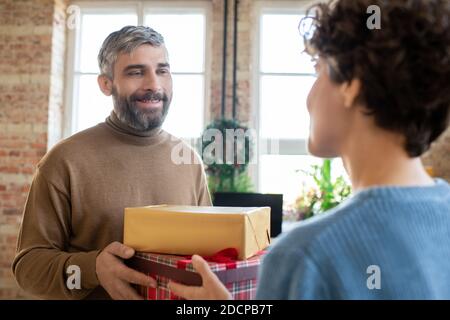 Felice uomo sopportato passando due doni a sua moglie mentre guardandola con sorriso Foto Stock