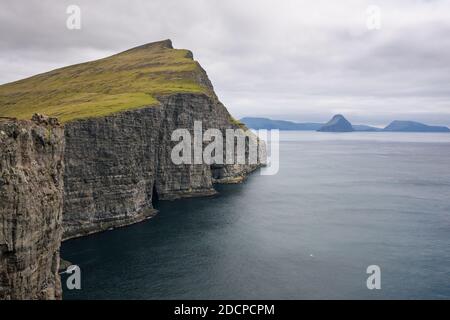 Vista spettacolare della ruvida scogliera con la verde collina situata nelle vicinanze mare sotto il cielo Foto Stock