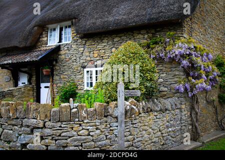 Un cottage storicamente significativo tetto di paglia con il cartello del sentiero di Coker Moor e glicine in East Coker, Somerset, Inghilterra Foto Stock