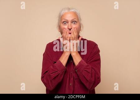 Donna anziana che è imbarazzata, ridendo coprendo la bocca con le mani Foto Stock