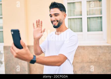 Giovane arabo sorridente felice di videochiamare con lo smartphone in città. Foto Stock