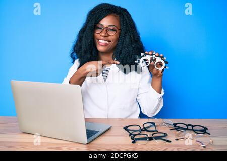 Bella donna africana che tiene occhiali di optometria sorridente felice indicando con mano e dito Foto Stock