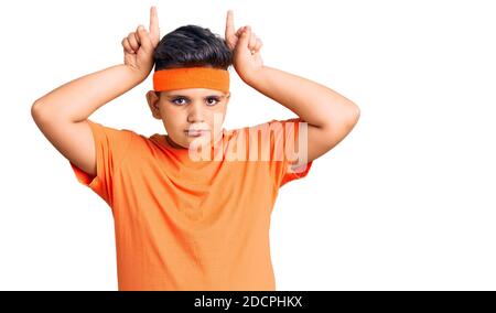 Bambino piccolo che indossa gli sportswear facendo il gesto divertente con le dita oltre la testa come corna toro Foto Stock