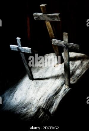 Una vista sfocata di tre croci di legno pugnate in un slab in un modello trinità all'interno di un interno scuro con luce che si illumina per il concetto spirituale Foto Stock