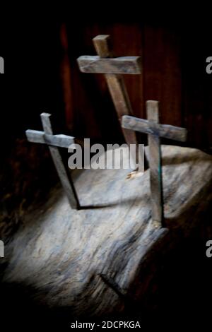 Una vista sfocata di tre croci di legno incastrate in una lastra in un modello trinità all'interno di un interno scuro con luce che si infondono per il concetto spirituale, Foto Stock