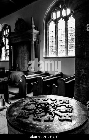 La bella luce della finestra in vetro con piombo si sprigola nell'interno della chiesa con banchi e fonte battesimale alla chiesa di St Michael & All Angels a East Coker, Inghilterra Foto Stock