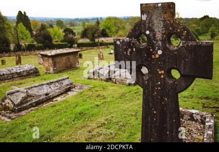 Primo piano di croce celtica in una parrocchia del Vecchio mondo Cimitero presso la chiesa di St Michael & All Angels con vista su un Paesaggio ondulato della campagna inglese Foto Stock