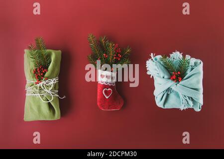 Festiva composizione di feltro decorativo calzino con rami di abete rosso e scatole regalo avvolte in tessuto e decorazioni naturali su ricco colore bordeaux Foto Stock