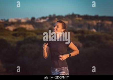 Atleta giovane e slim da donna che corre con tracker per il fitness o orologio intelligente. Corsa con le cuffie Foto Stock