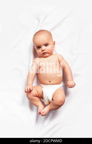 Caucasico divertente bambino in pannolino bianco giace su sfondo chiaro. Vista dall'alto. Igiene dei bambini, cambio pannolino e cura della pelle del bambino. Foto Stock