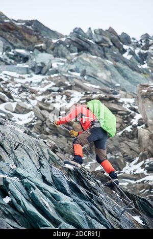 Coraggioso alpinista che tiene la corda mentre sale cresta alpina. Giovane arrampicatore con zaino ascendente montagna e cercando di raggiungere la vetta. Concetto di alpinismo, alpinismo e alpinismo. Foto Stock