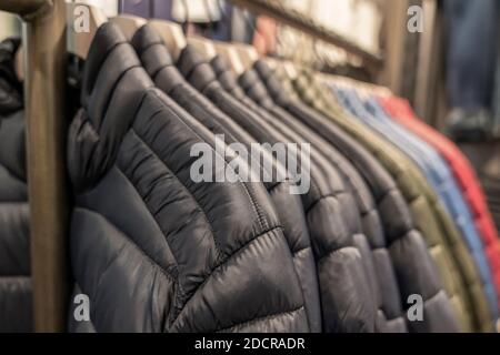 Le giacche calde dell'autunno e dell'inverno degli uomini giù giubbotti ordinatamente appendono in una fila in un deposito dell'abbigliamento su un appendiabiti. Foto Stock