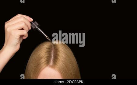 Capelli rosso chiaro donna su fondo nero e una pipetta con olio cosmetico. Cura dei capelli e del cuoio capelluto. Foto Stock