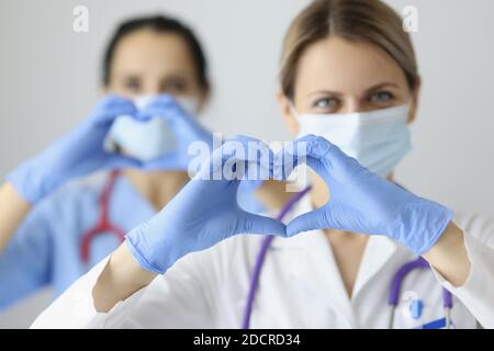 Due medici in maschere mediche e guanti di gomma che mostrano il cuore con le mani Foto Stock