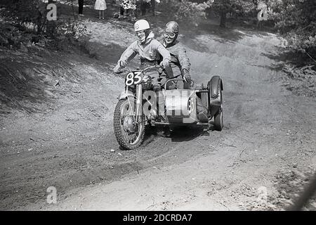 Alla fine degli anni '50, un concorrente maschile in un evento di scrambling motociclistico, che attraversa un sentiero fangoso. Inventata nel 1924, a Camberley, Surrey, in Inghilterra, le moto usate per la corsa negli anni '50 e all'inizio degli anni '60 erano poco diverse dalle moto da strada del tempo, con pochissime sospensioni. Oggi lo sport è conosciuto come motocross – il nome francese per il cross-country motociclismo – e chiamato Supercross negli Stati Uniti. Foto Stock